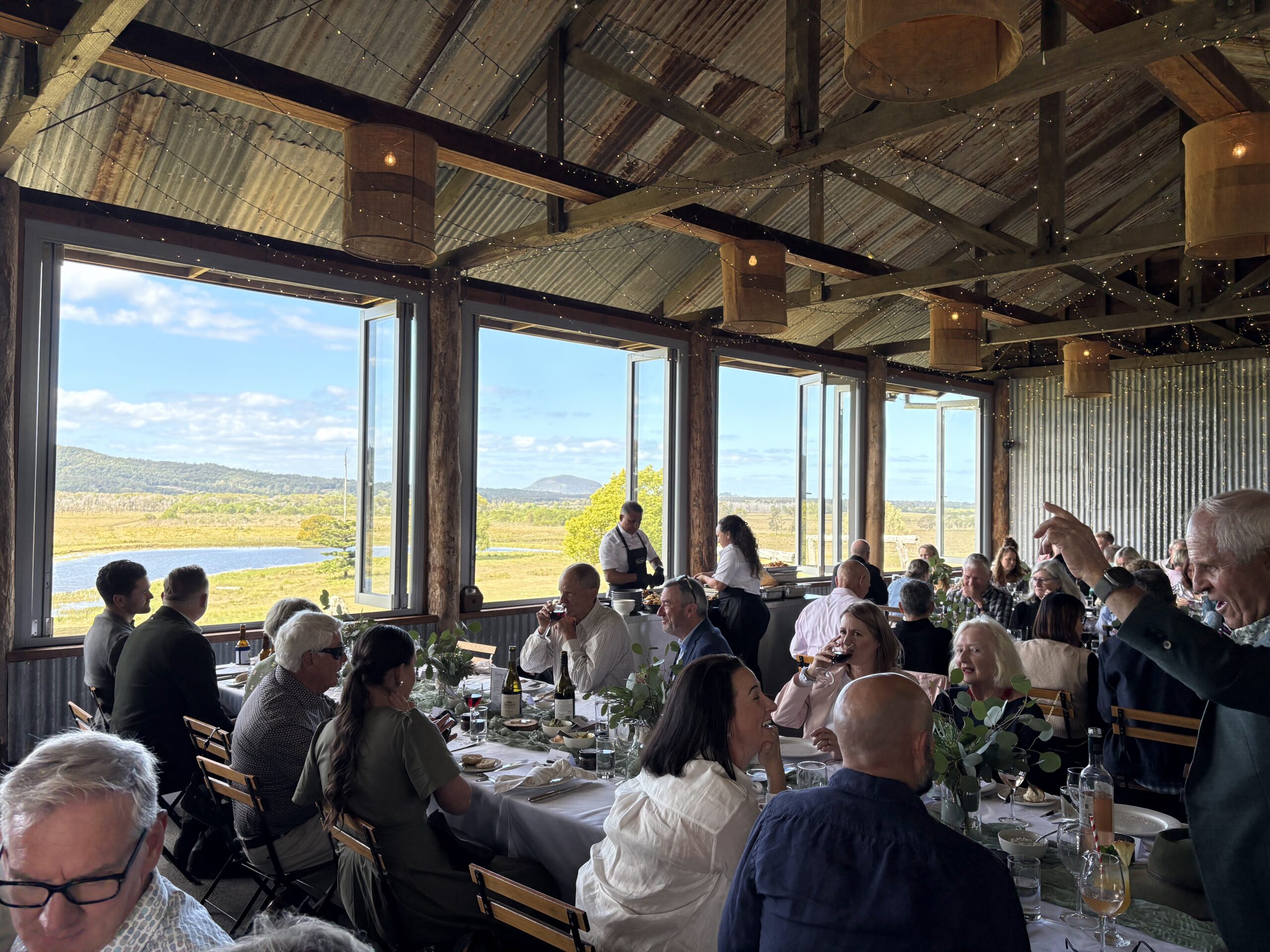 Guests dining at long tables with the windows open onto the valley