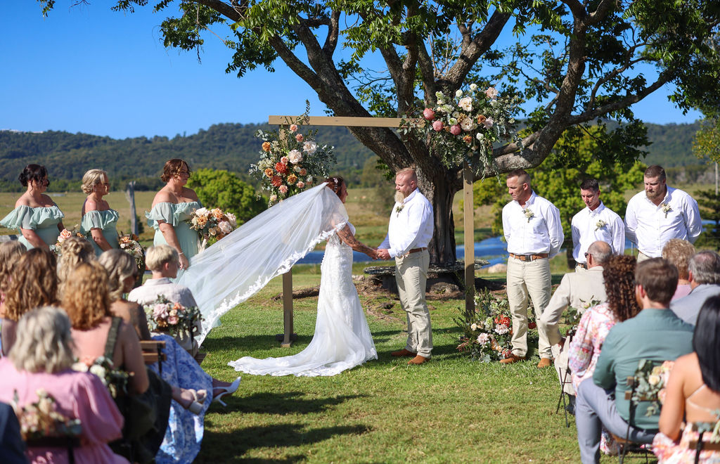 A couple at the altar beneath a Moreton Bay Fig, guests seated on the grass