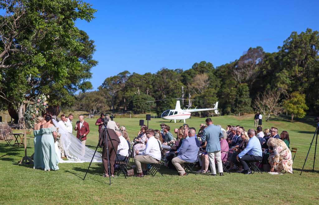 A ceremony on the open lawn, guests seated in the sun, the hinterland ranges behind