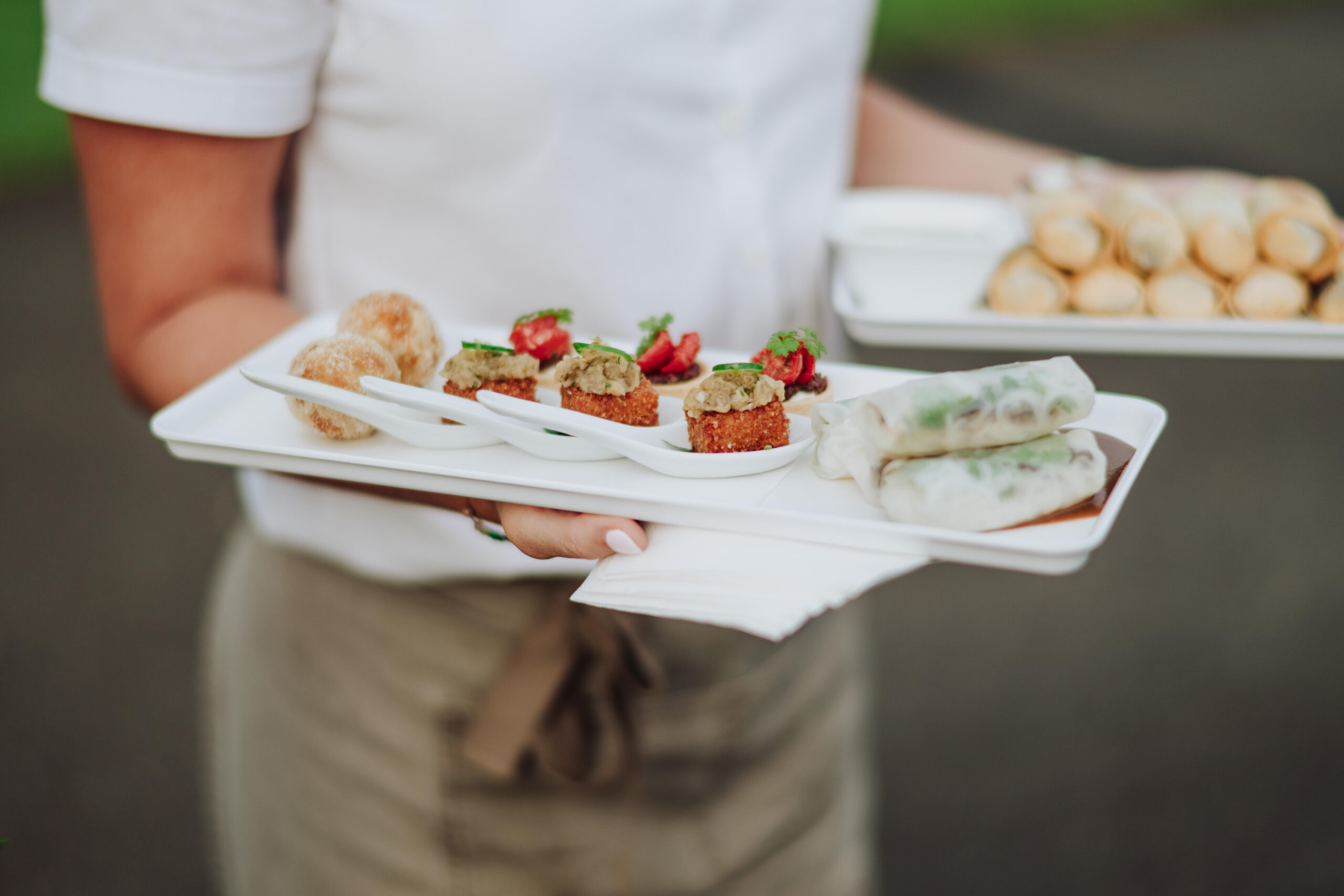 A server carrying a tray of canapes across the lawn
