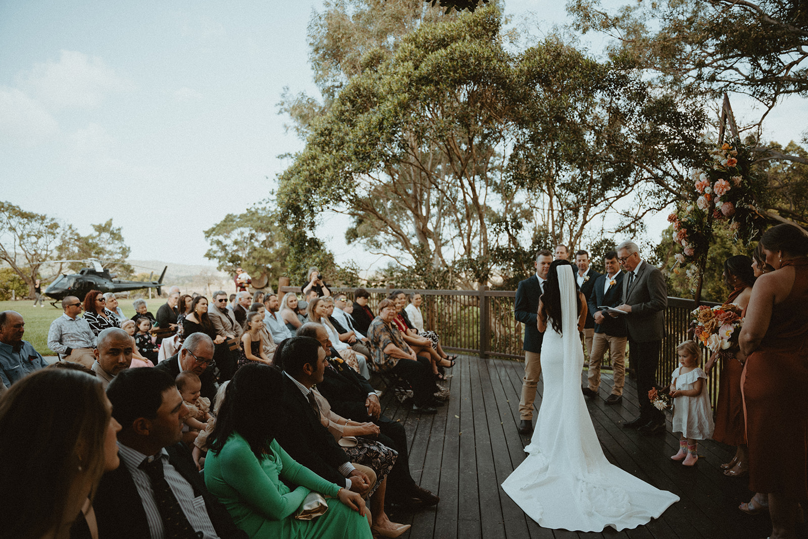 A bride walking the aisle between seated guests under tall gum trees