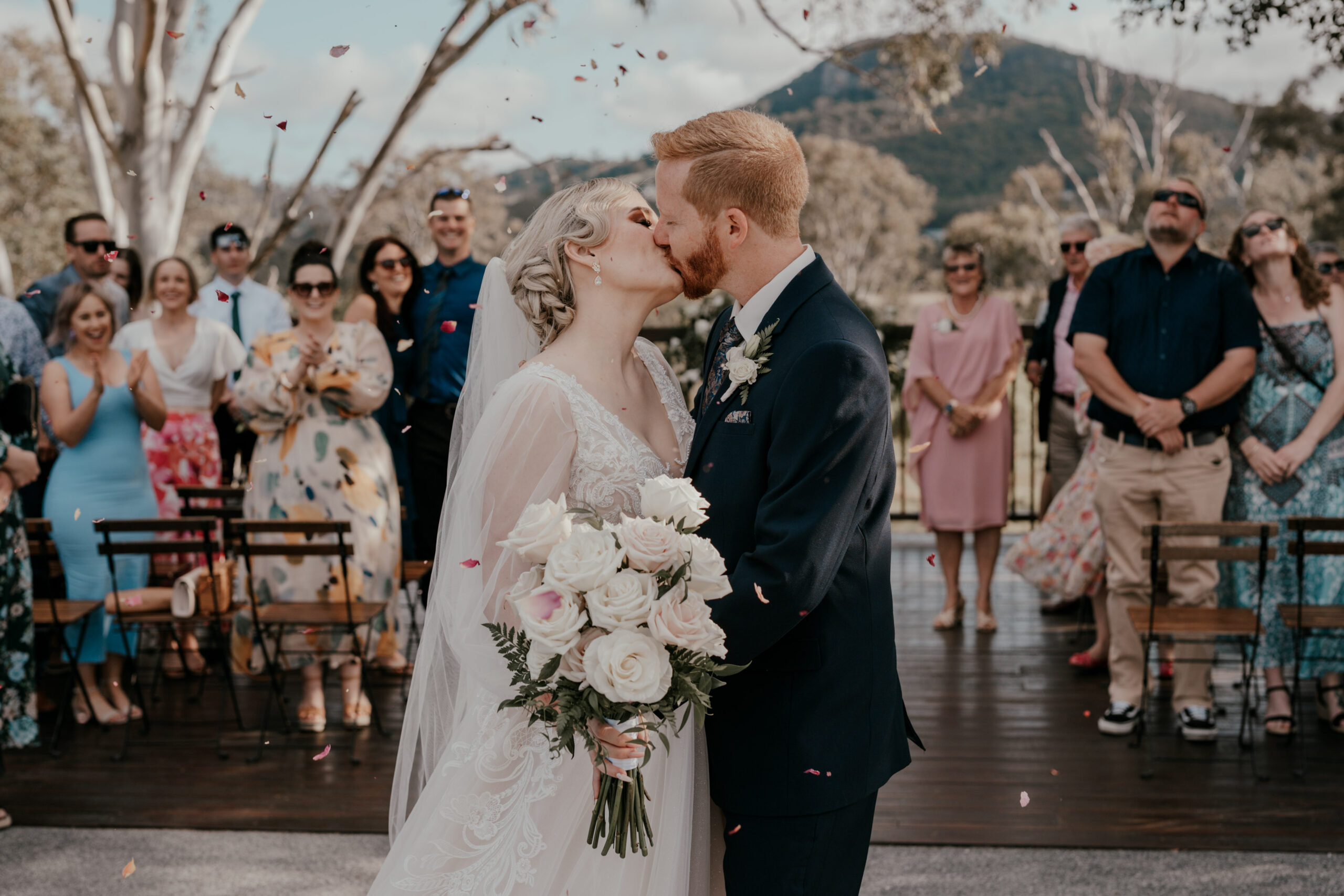 A couple kissing at the end of the ceremony, guests applauding around them