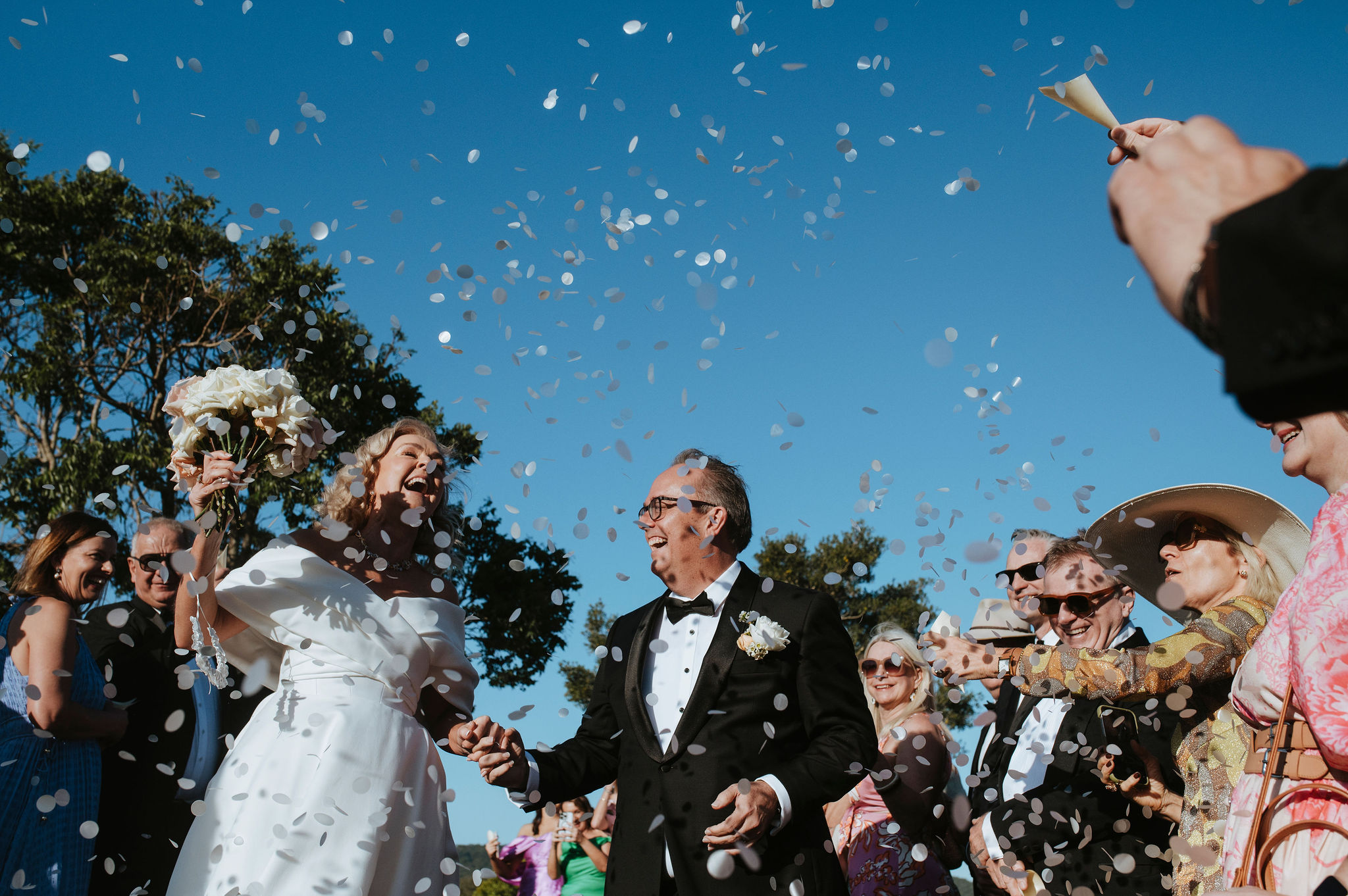 Confetti thrown over a couple against a clear blue sky