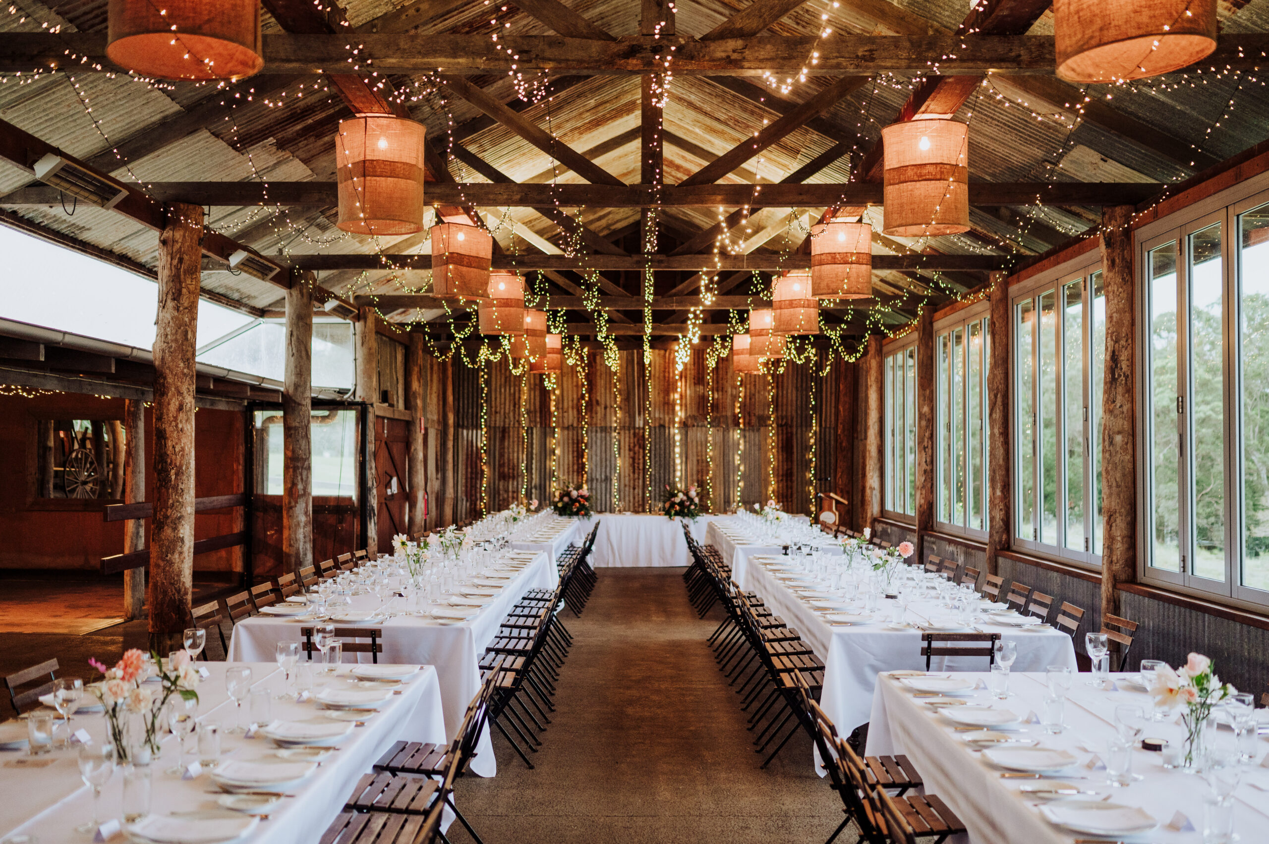 Long banquet tables set in the Dairy Barn beneath a canopy of festoon lights