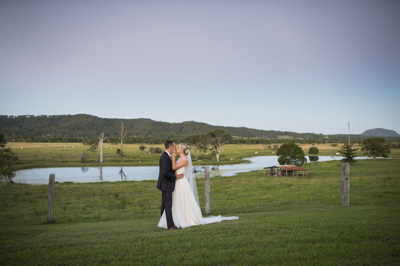 A couple photographed at dusk with the property behind them