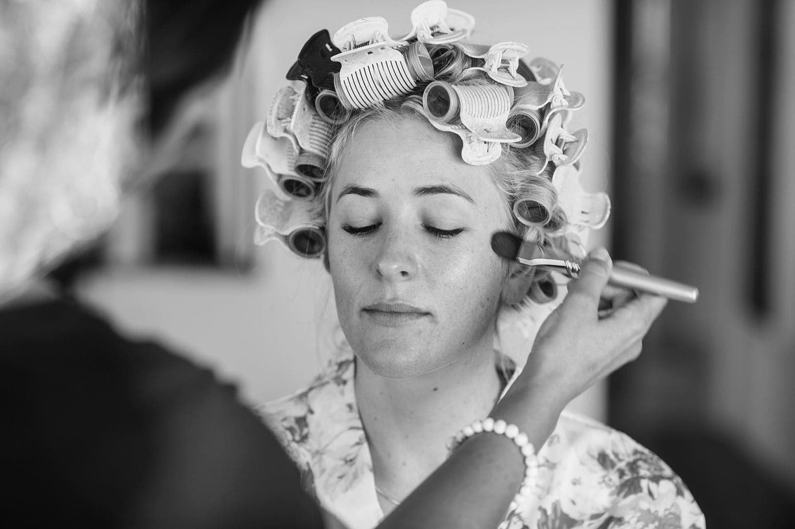 A bride having her makeup done, hair in rollers, eyes closed