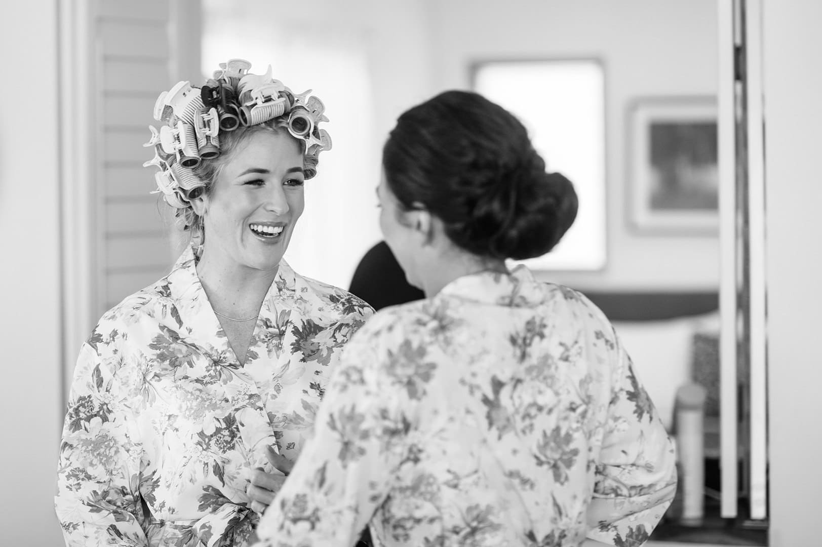 Two women laughing together during hair and makeup in a cottage room