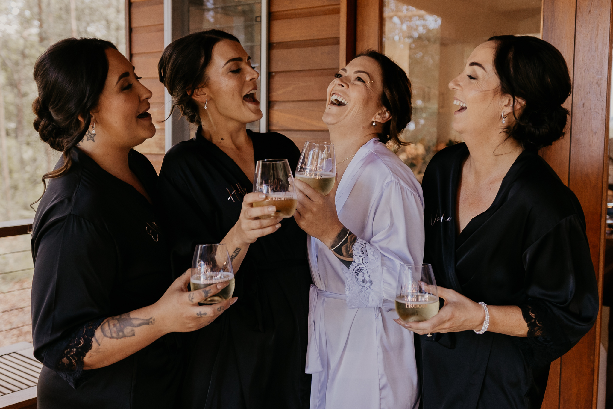 Four women in satin robes laughing with wine glasses on a timber cottage deck