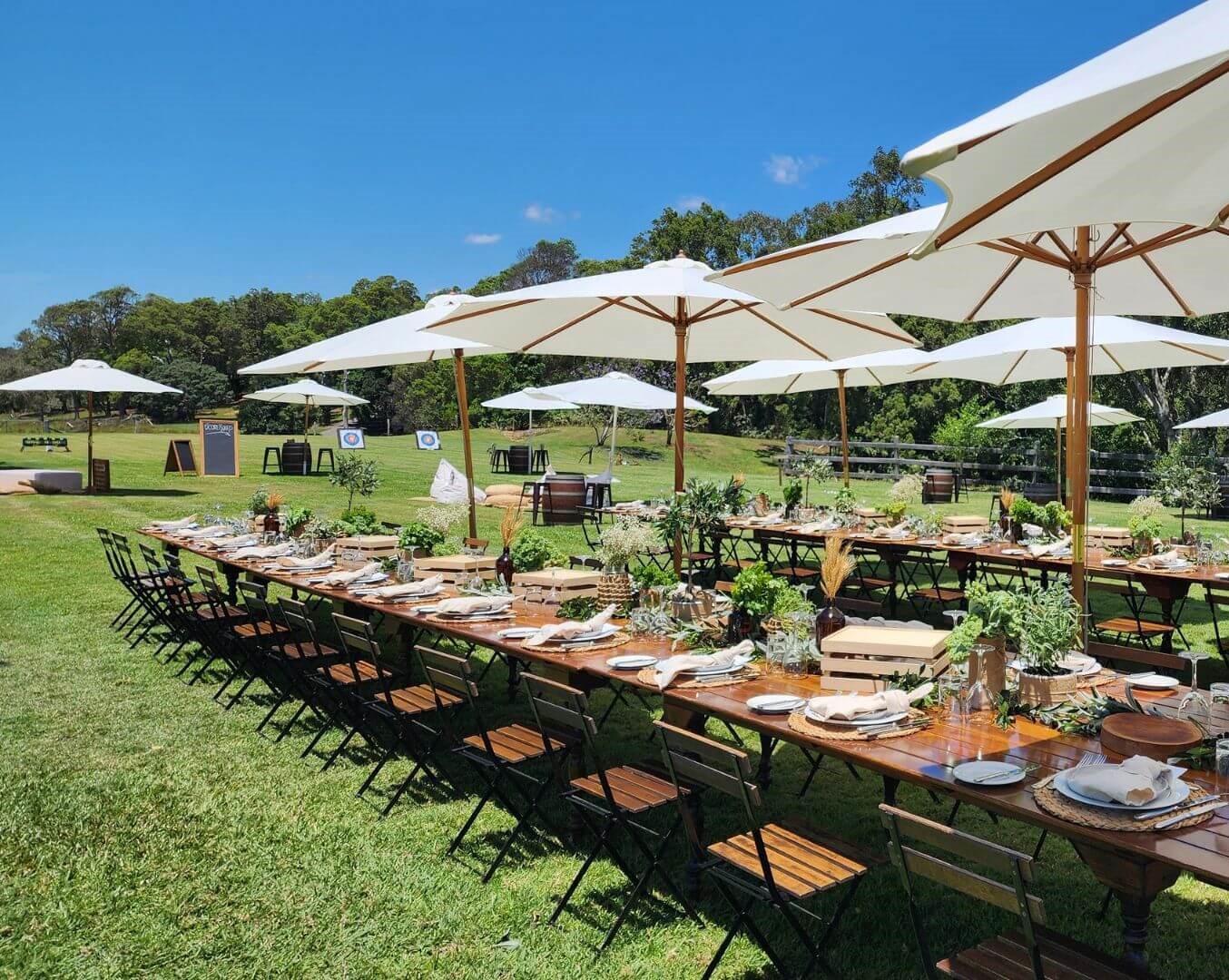 A long banquet table set on the lawn under white umbrellas